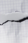 A piece of graph paper with a central horizontal tear revealing the same paper beneath. The grid pattern on the paper is visible, with the tear edges appearing slightly rough.