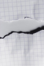 A piece of graph paper with a central horizontal tear revealing the same paper beneath. The grid pattern on the paper is visible, with the tear edges appearing slightly rough.