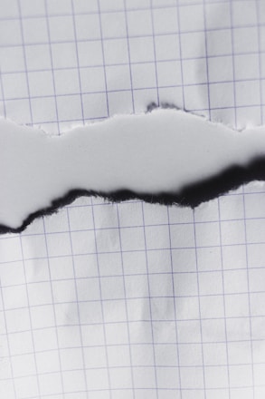 A piece of graph paper with a central horizontal tear revealing the same paper beneath. The grid pattern on the paper is visible, with the tear edges appearing slightly rough.