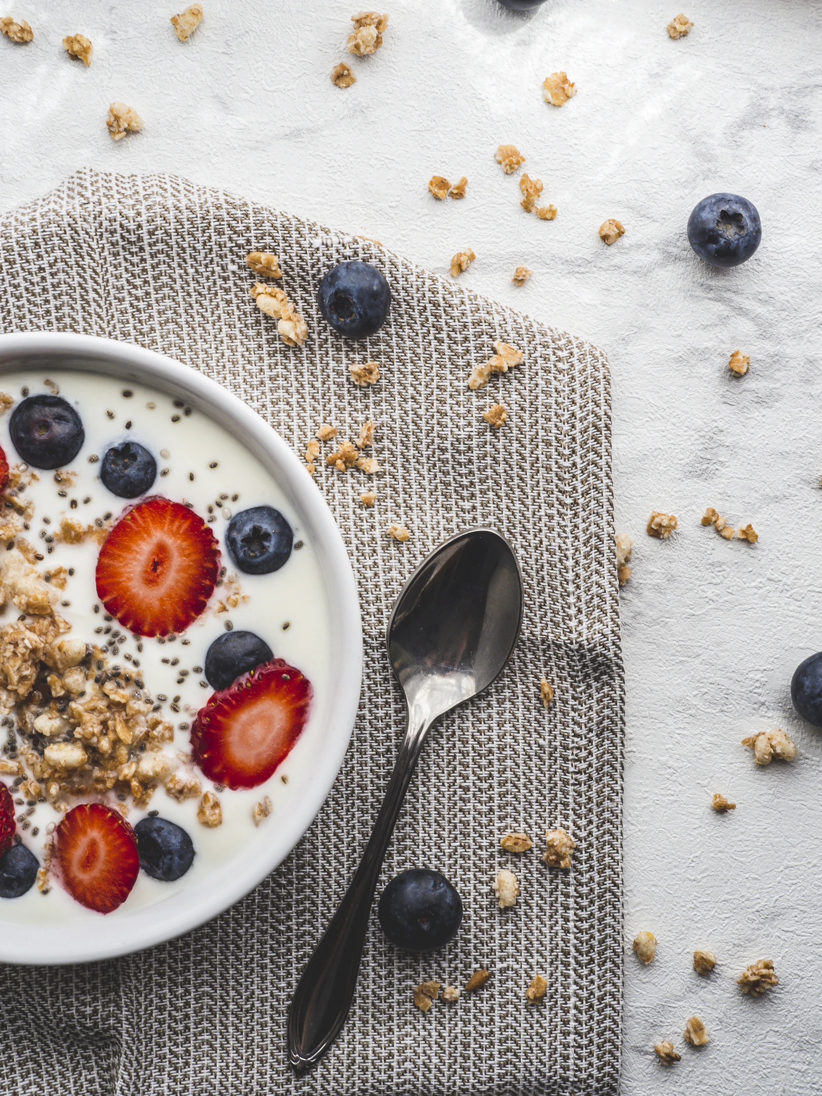 Bol de yaourt garni de granola, fraises et myrtilles sur un set de table en lin