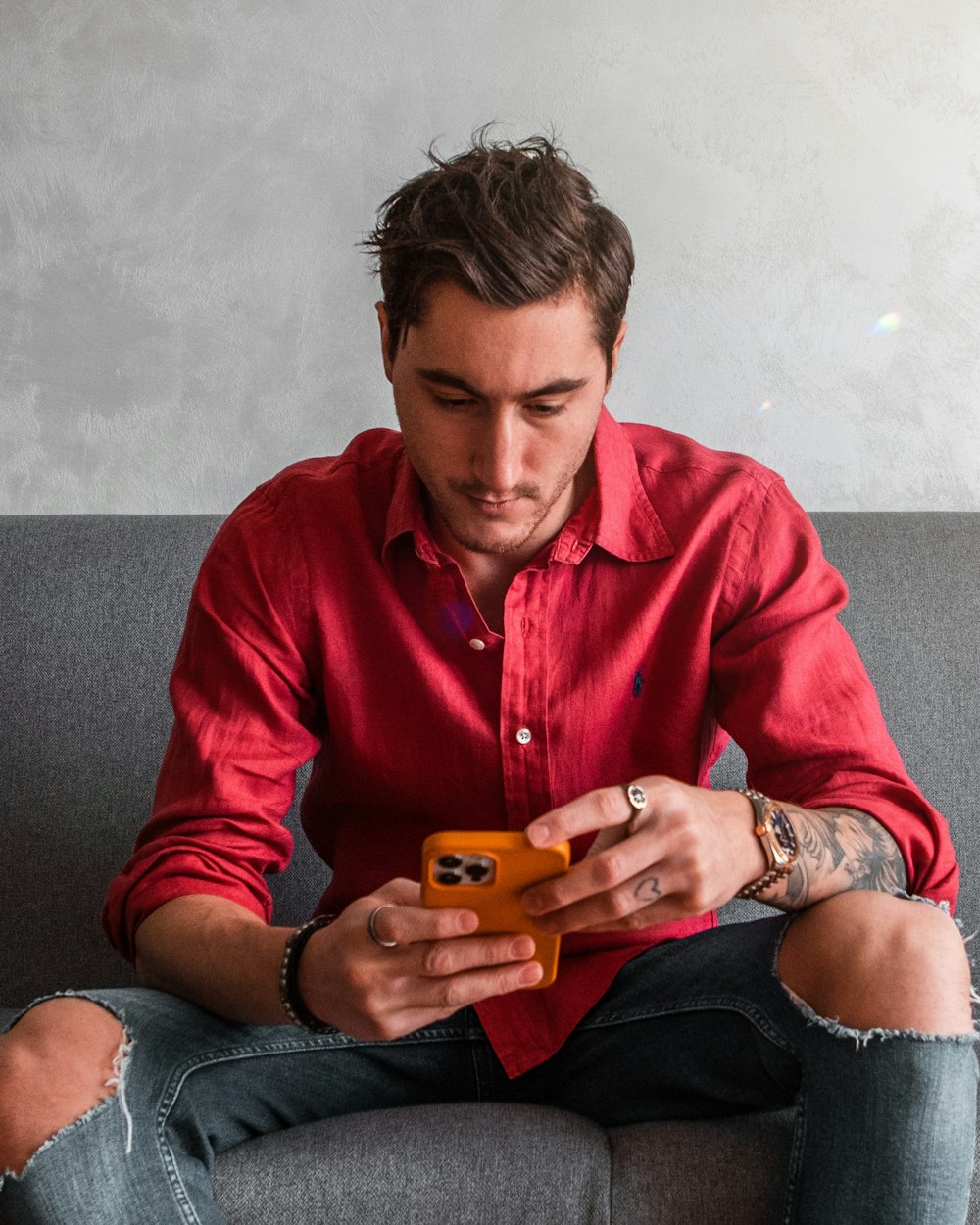 woman in red dress shirt and blue denim jeans sitting on black couch