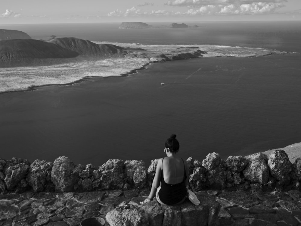 woman in black tank top sitting on rock formation in grayscale photography