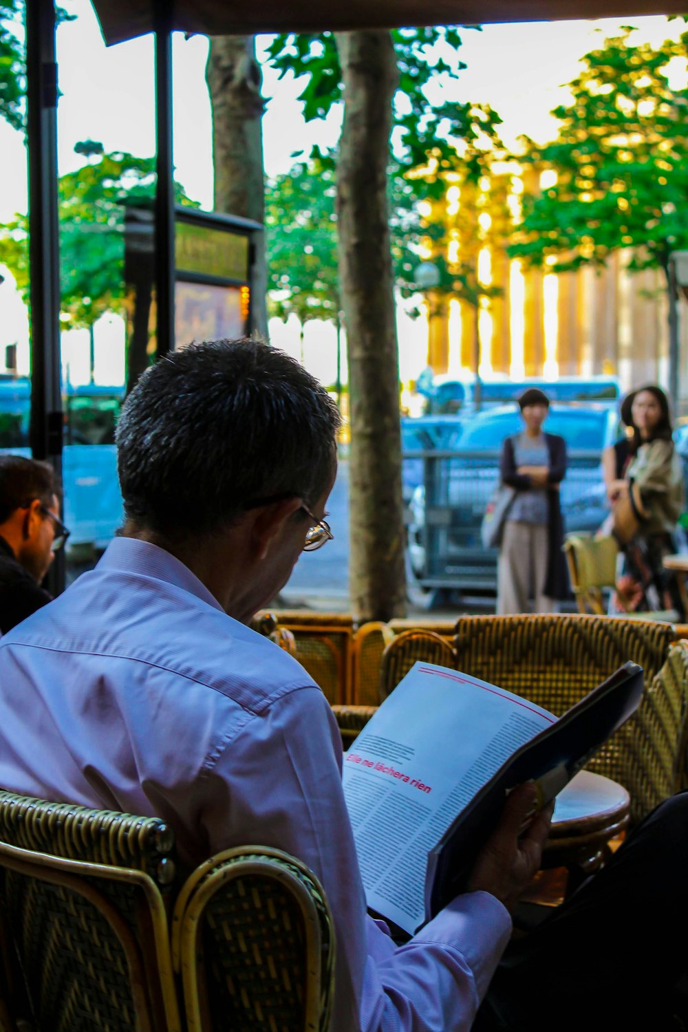 man in white dress shirt sitting on brown wicker chair reading book