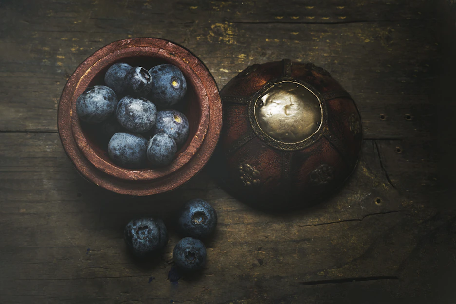Close-up of fresh blueberries and a bottle of artisanal blueberry wine on rustic wooden table