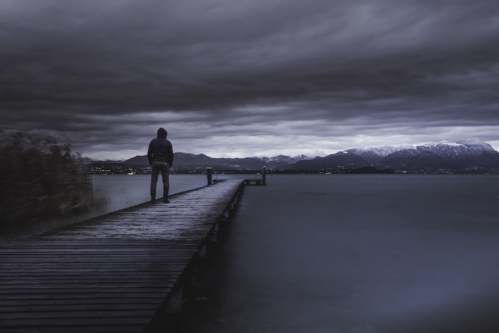 man in black jacket standing on wooden dock