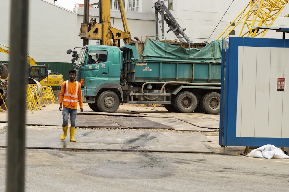 man in yellow shirt and blue denim jeans standing beside green and blue truck