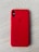 A smartphone with a red protective case resting on a light wooden surface. The case features a brand logo subtly embossed in the center. The camera lenses are visible on the top left corner of the case.