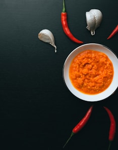 soup in white ceramic bowl beside red handled spoon and fork on black table