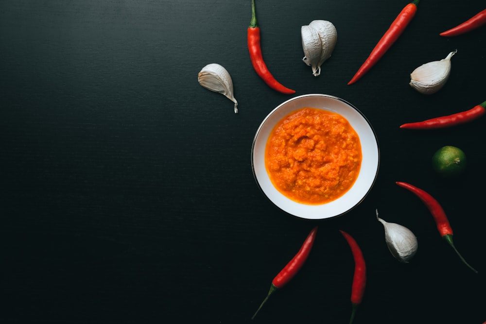 sopa en un cuenco de cerámica blanca junto a una cuchara y un tenedor con mango rojo en una mesa negra