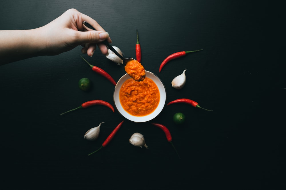 person holding red and silver fork and red chili pepper on white ceramic bowl