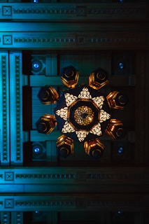 A geometric ceiling design with intricate wooden carvings and a central decorative chandelier featuring illuminated, ornate patterns.