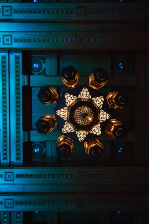 A geometric ceiling design with intricate wooden carvings and a central decorative chandelier featuring illuminated, ornate patterns.