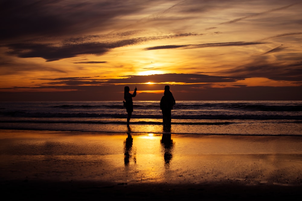 silhouette of 2 person standing on beach during sunset