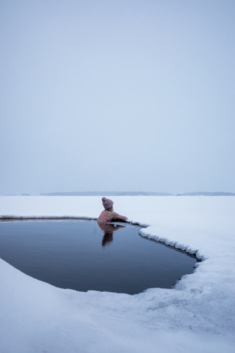 Person relaxing in an outdoor cold plunge pool surrounded by snow and winter landscape