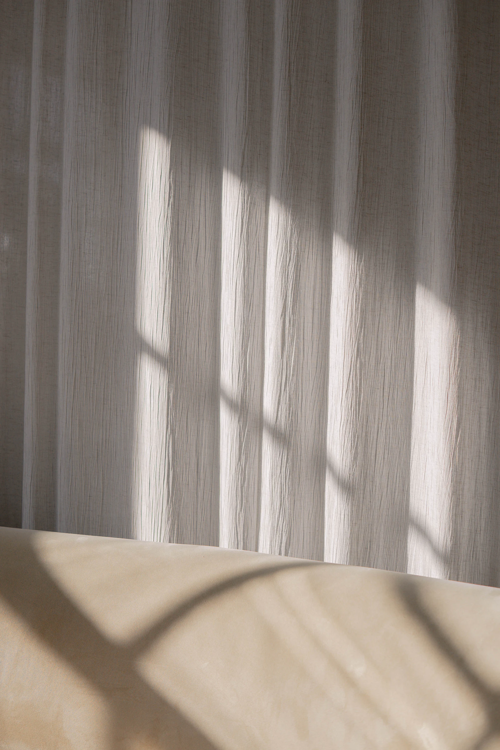 Sheer curtain diffusing daylight across a plain interior wall