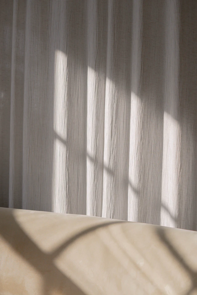Sheer curtain diffusing daylight across a plain interior wall