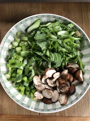 Close-up of a matte forest green bowl filled with vibrant seasonal vegetables.