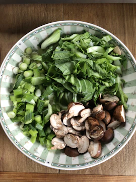 Close-up of a matte forest green bowl filled with vibrant seasonal vegetables.
