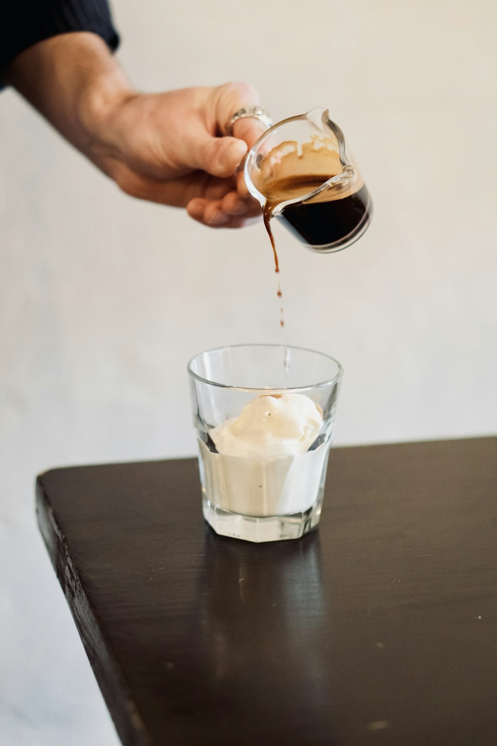 person pouring brown liquid on clear drinking glass