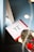 A greeting card with 'love you' written on it is adorned with small red heart patterns. It rests on a blue surface beside a silver, textured object with red rose petals. Warm, soft lighting from out-of-focus lights creates a cozy ambiance.