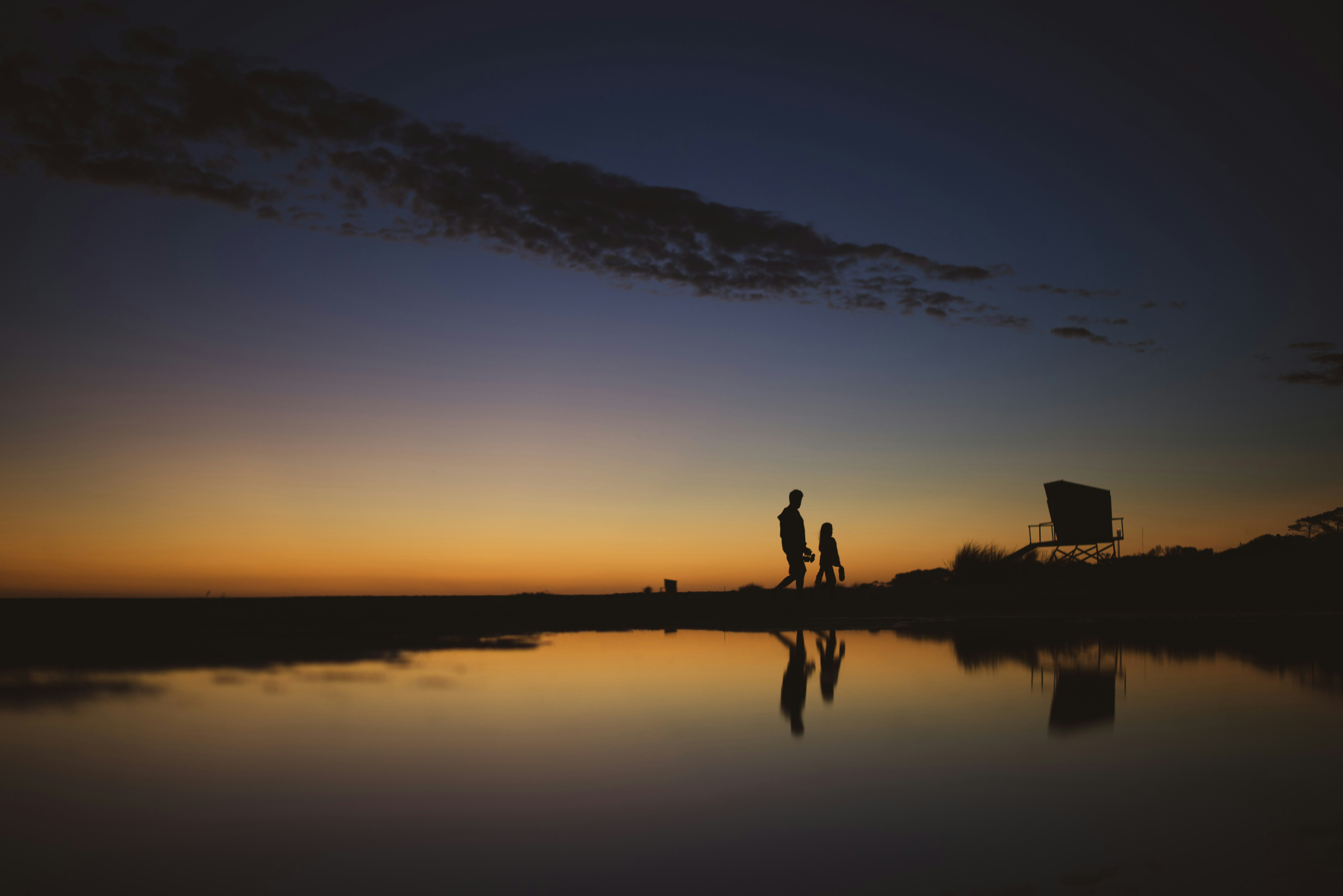 silhouette of 2 person standing on body of water during sunset