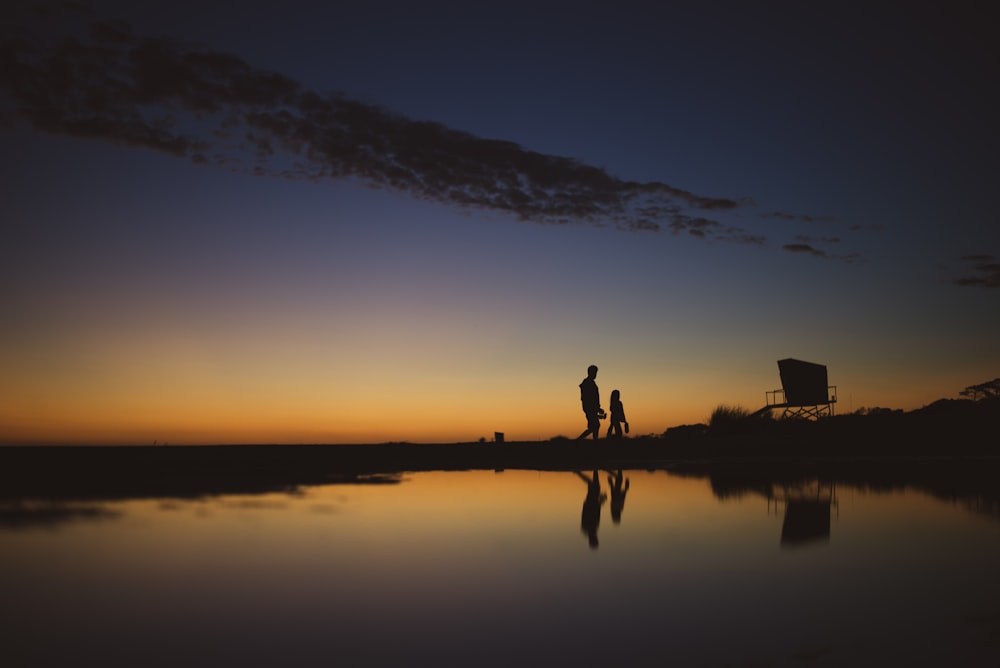 silhouette of 2 person standing on body of water during sunset