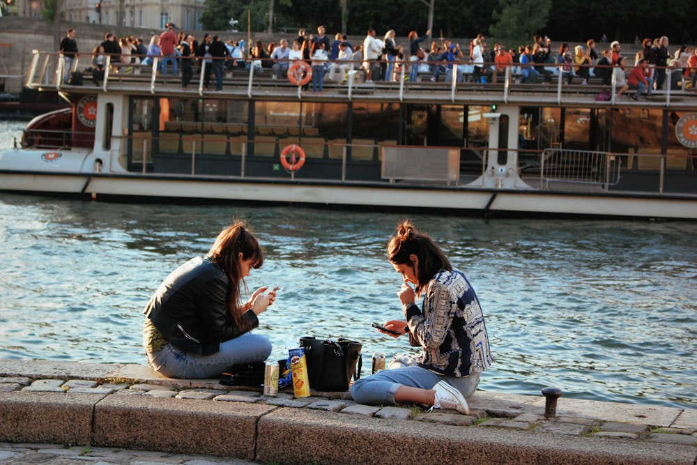 2 femmes assises sur un banc en béton près d’un plan d’eau pendant la journée