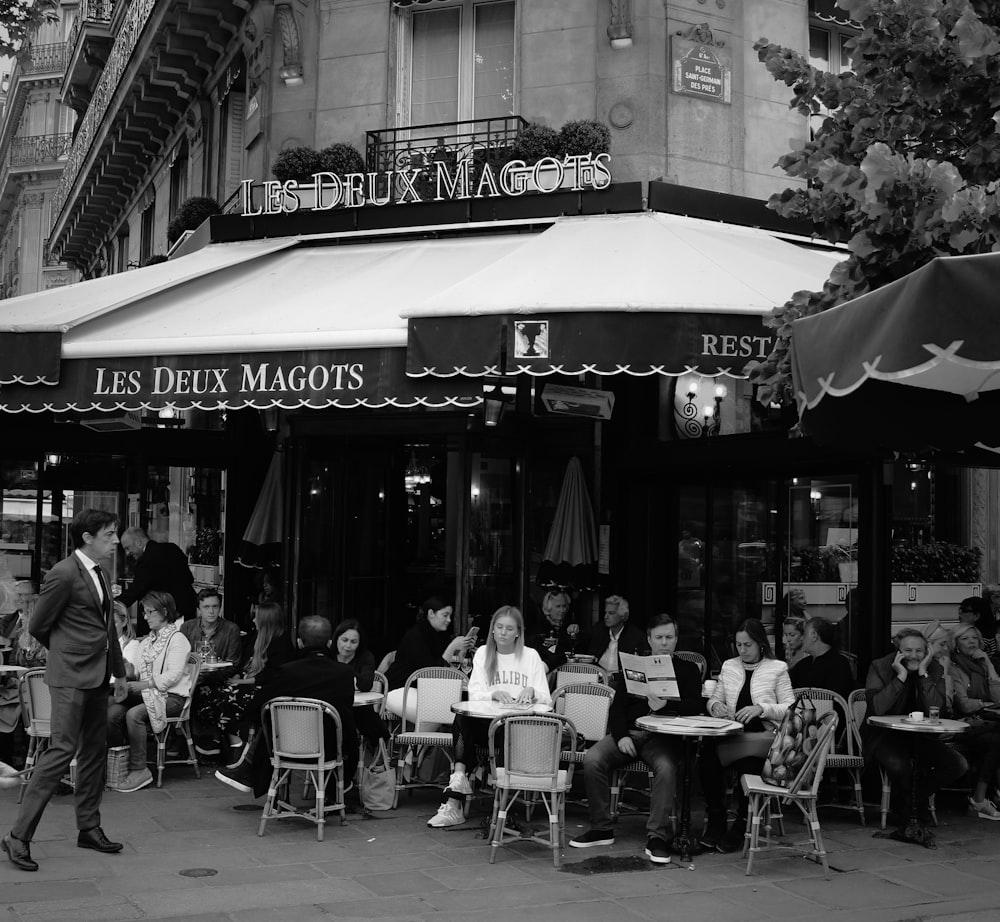 grayscale photo of people sitting on chairs near building