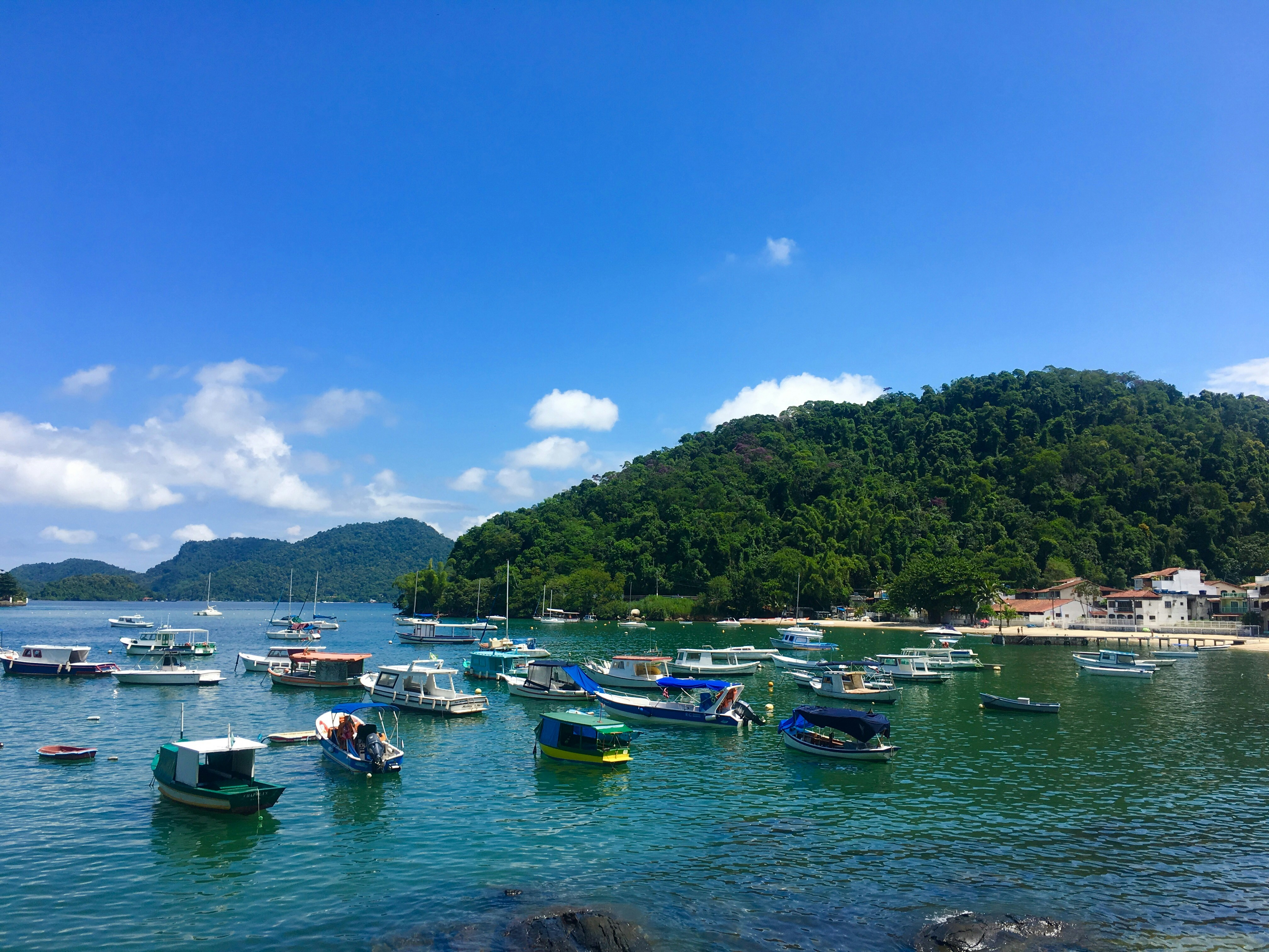 boats on body of water near green mountain under blue sky during daytime