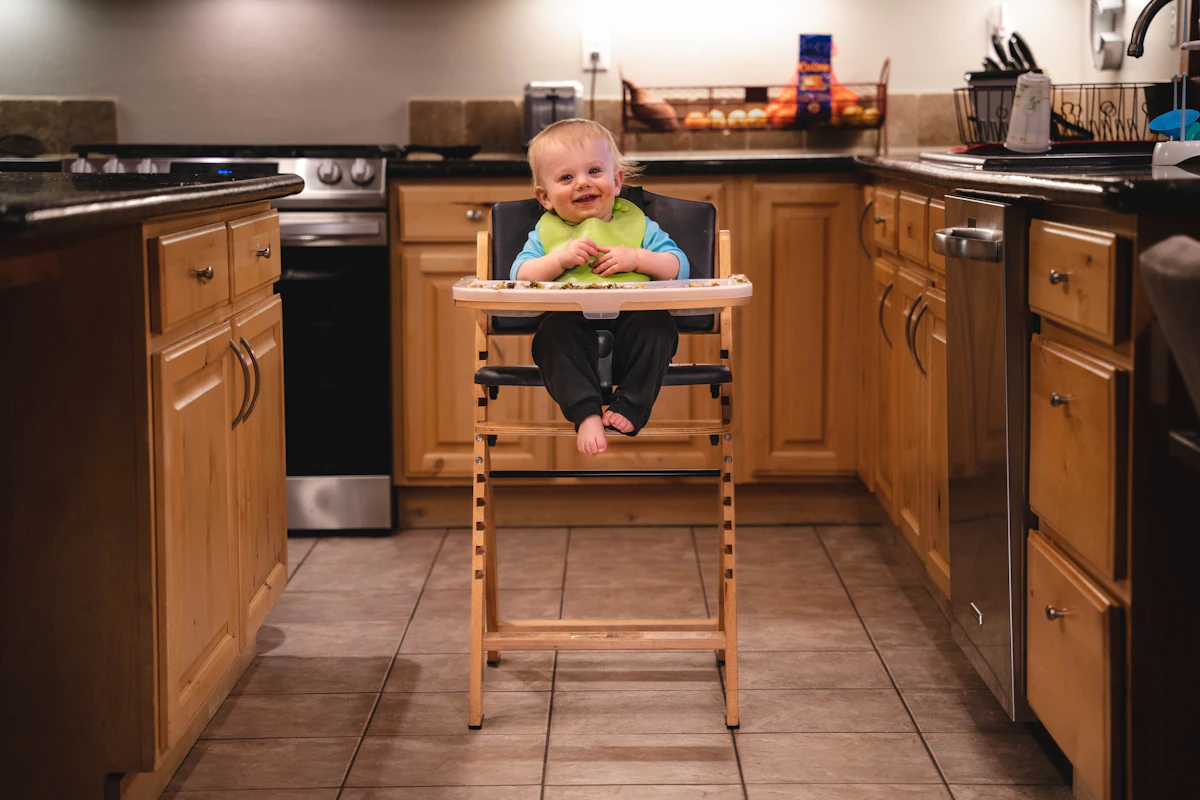 A baby in a standalone wooden high chair with its own floor stand in a home kitchen