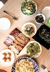 carne fatiada em prato de cerâmica branca ao lado de salada de legumes verde em tigela de cerâmica b