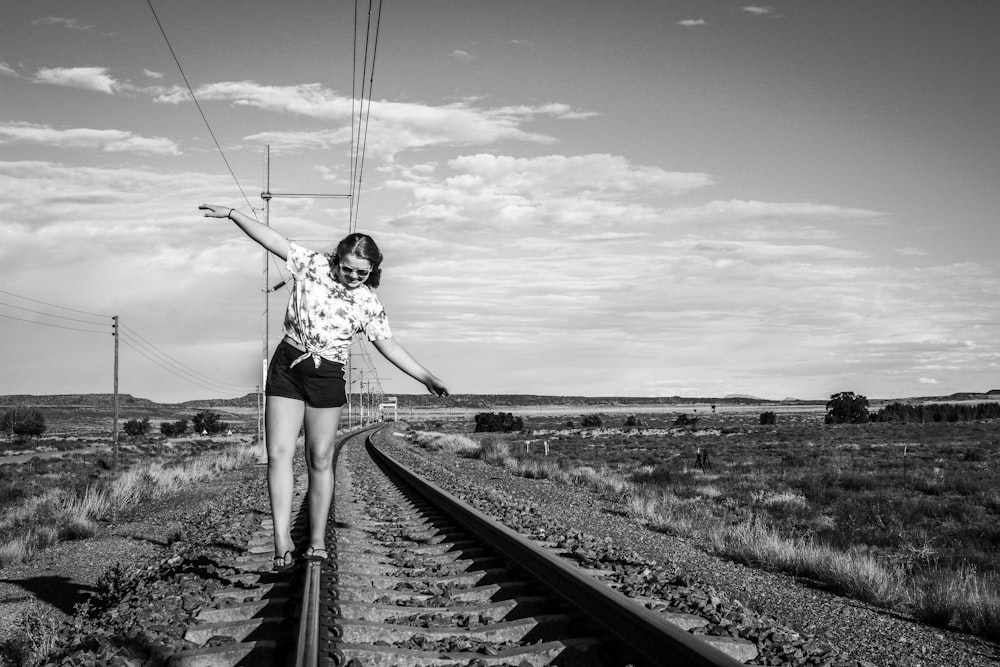 woman in white shirt and black shorts standing on train rail