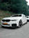 A happy customer standing next to a sleek white self-drive car with a scenic beach backdrop.