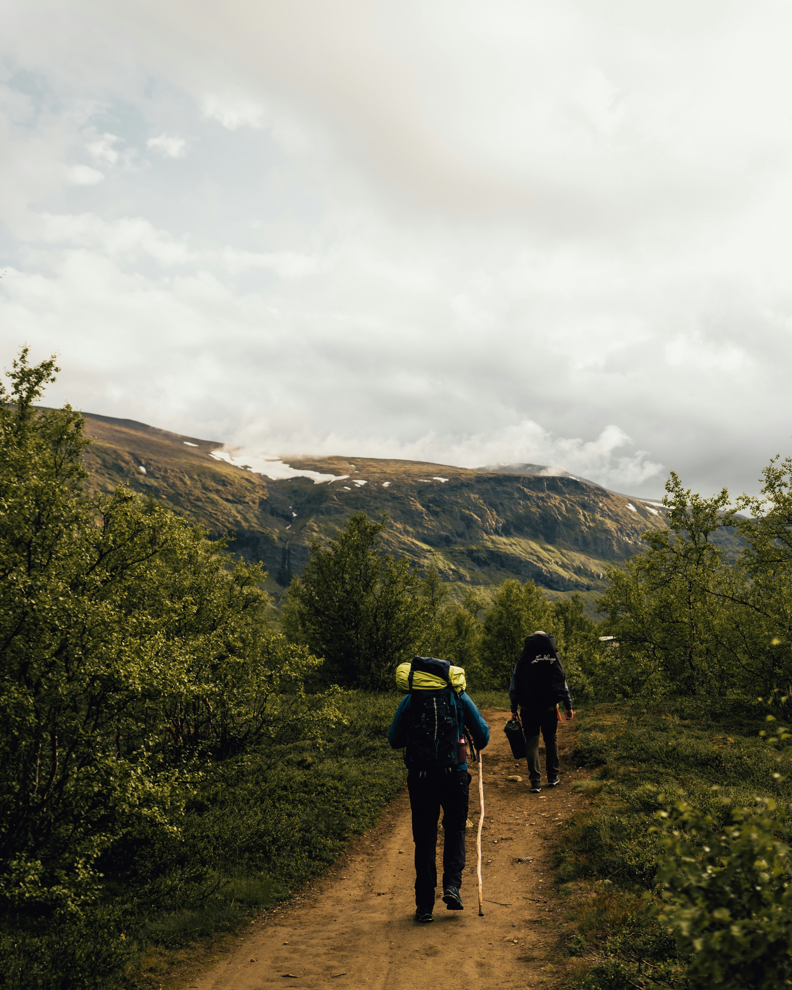 2 person walking on dirt road near green grass field during daytime