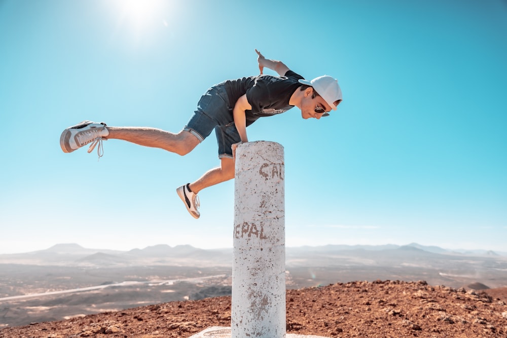 man in black t-shirt and white cap jumping on brown wooden post during daytime