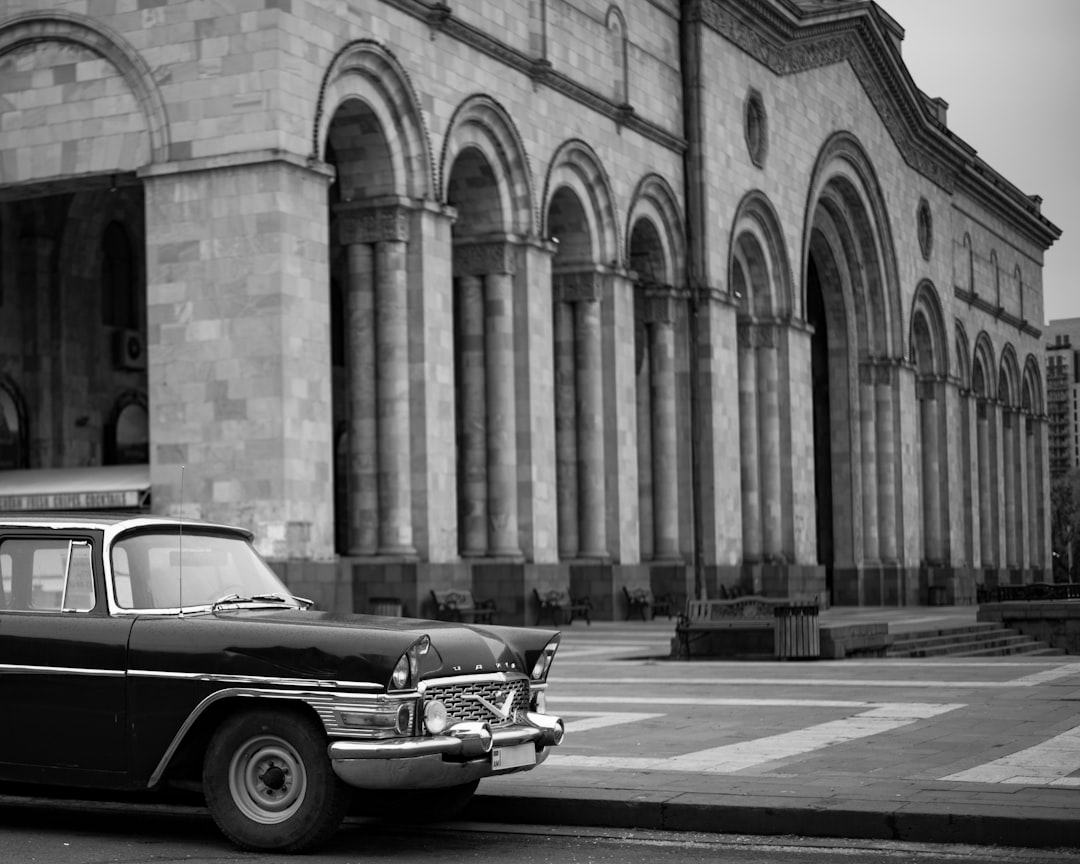 grayscale photo of classic car parked beside building