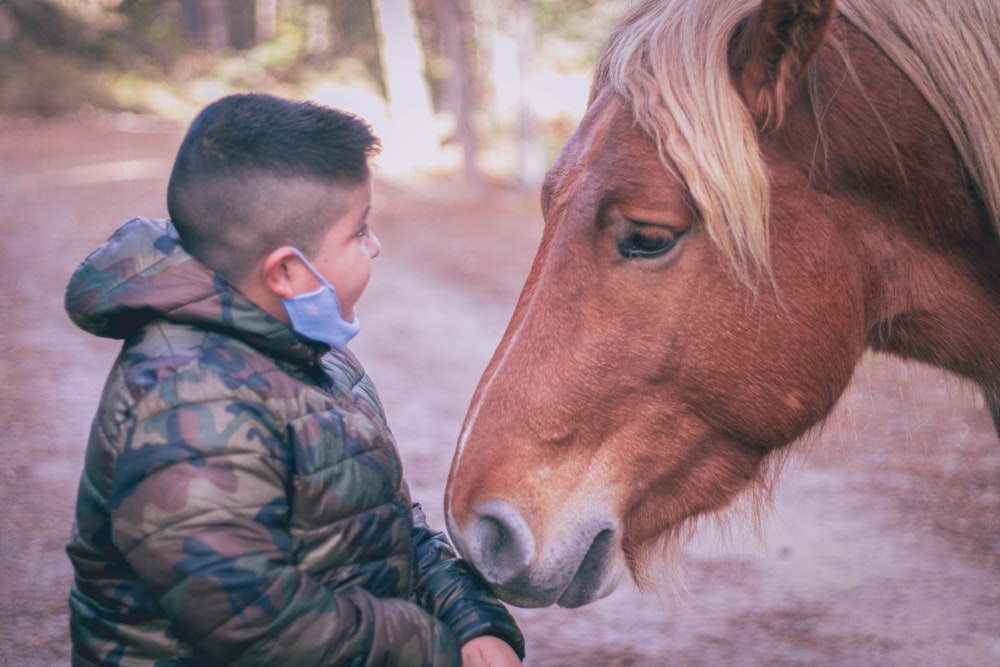 man in black and green camouflage jacket beside brown horse during daytime