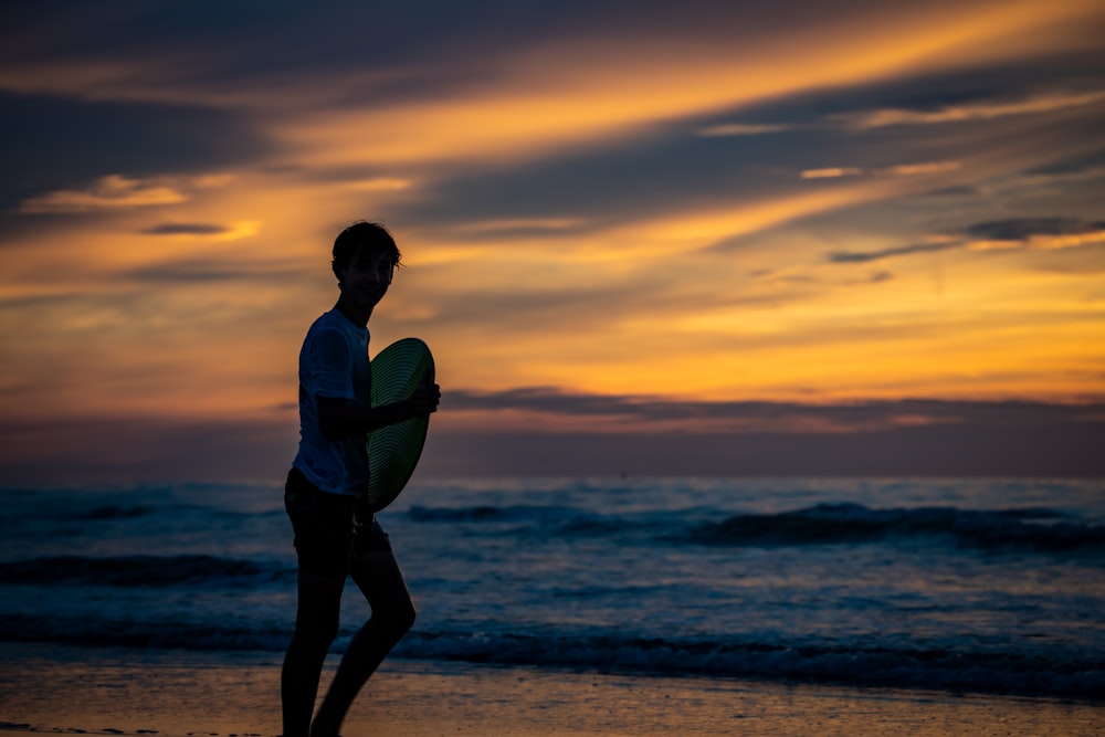 woman in white shirt and black pants holding white surfboard on beach during sunset