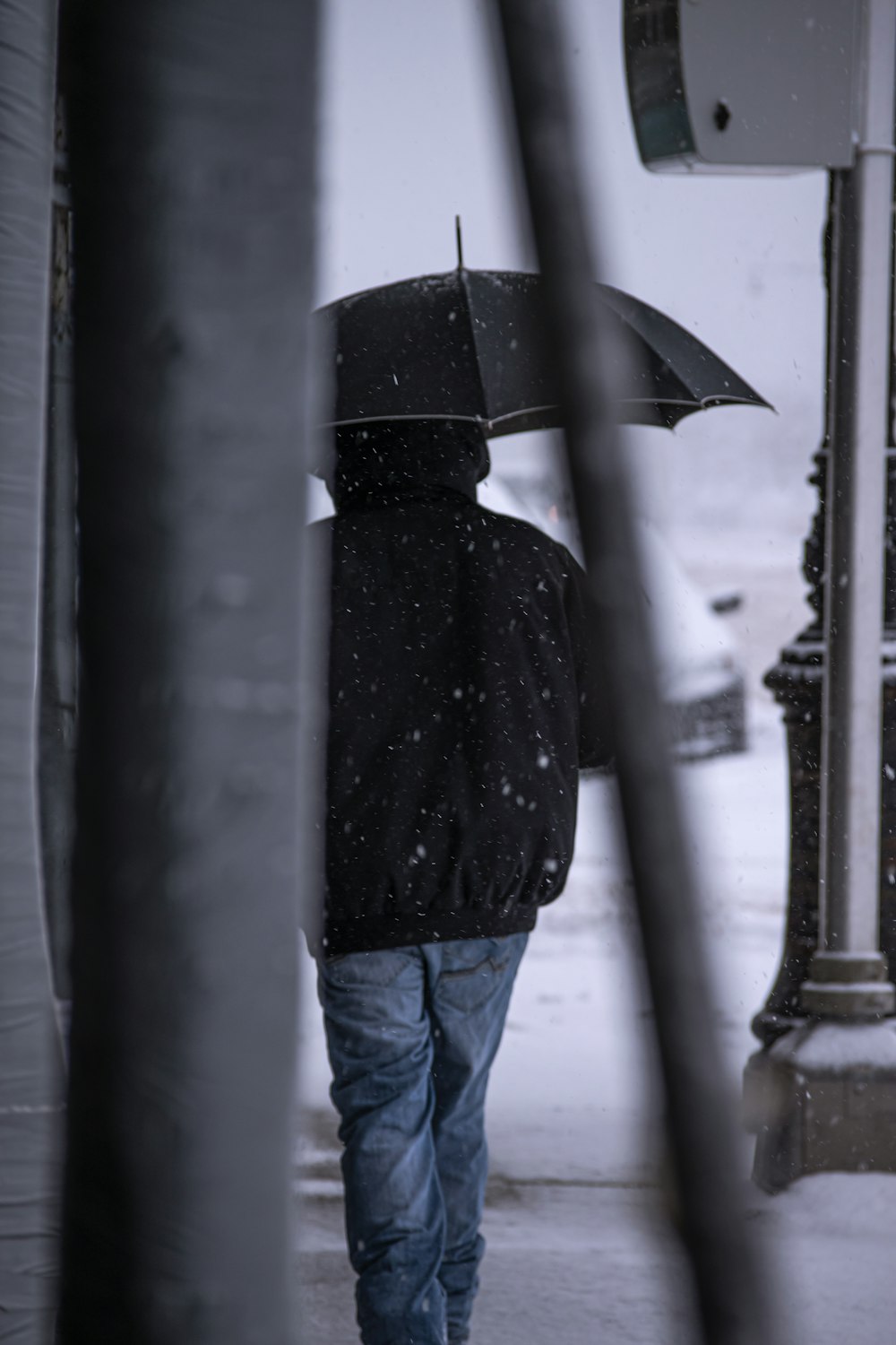person in black coat and blue denim jeans holding umbrella