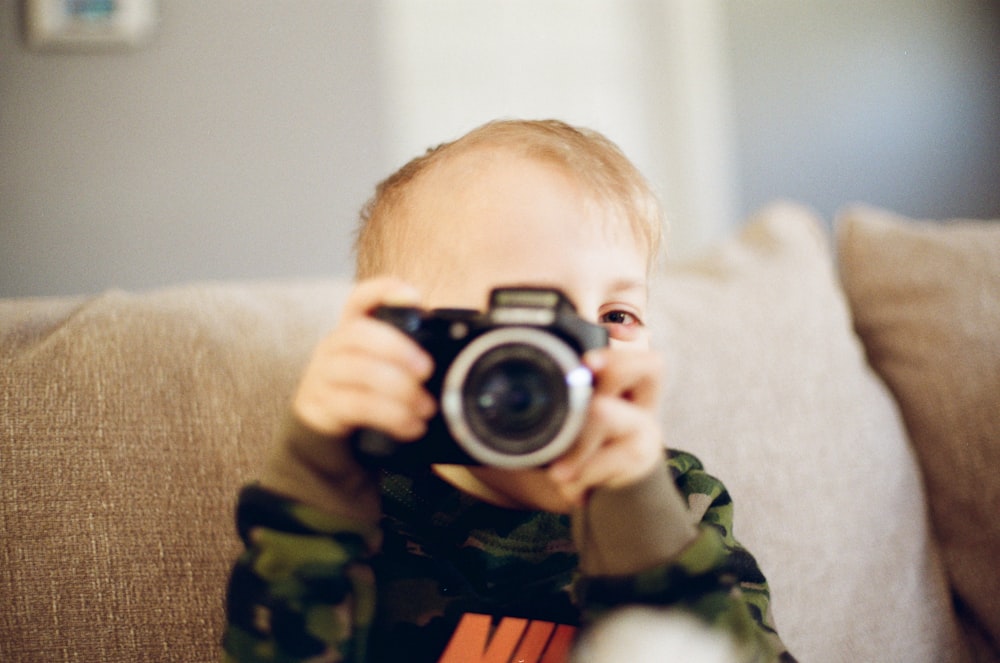 boy in green and black camouflage jacket holding black and silver camera