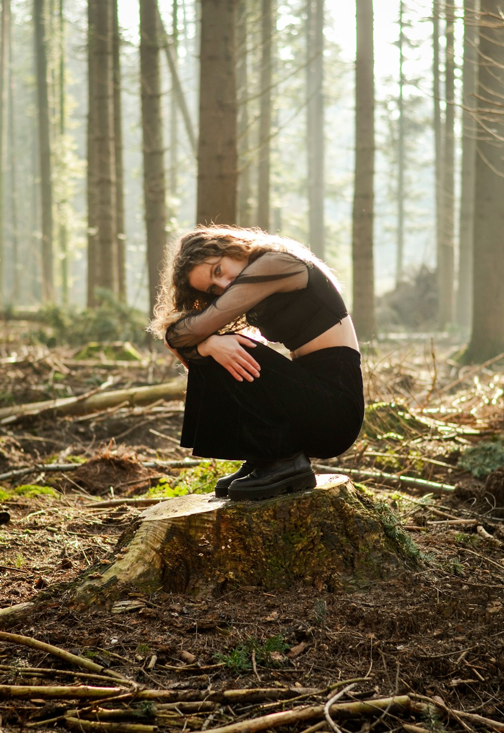 woman in black dress sitting on brown tree log during daytime