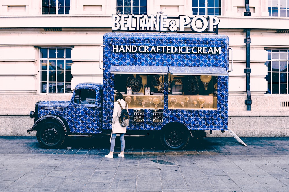 man in white shirt and black pants standing beside blue and white UNKs restaurant