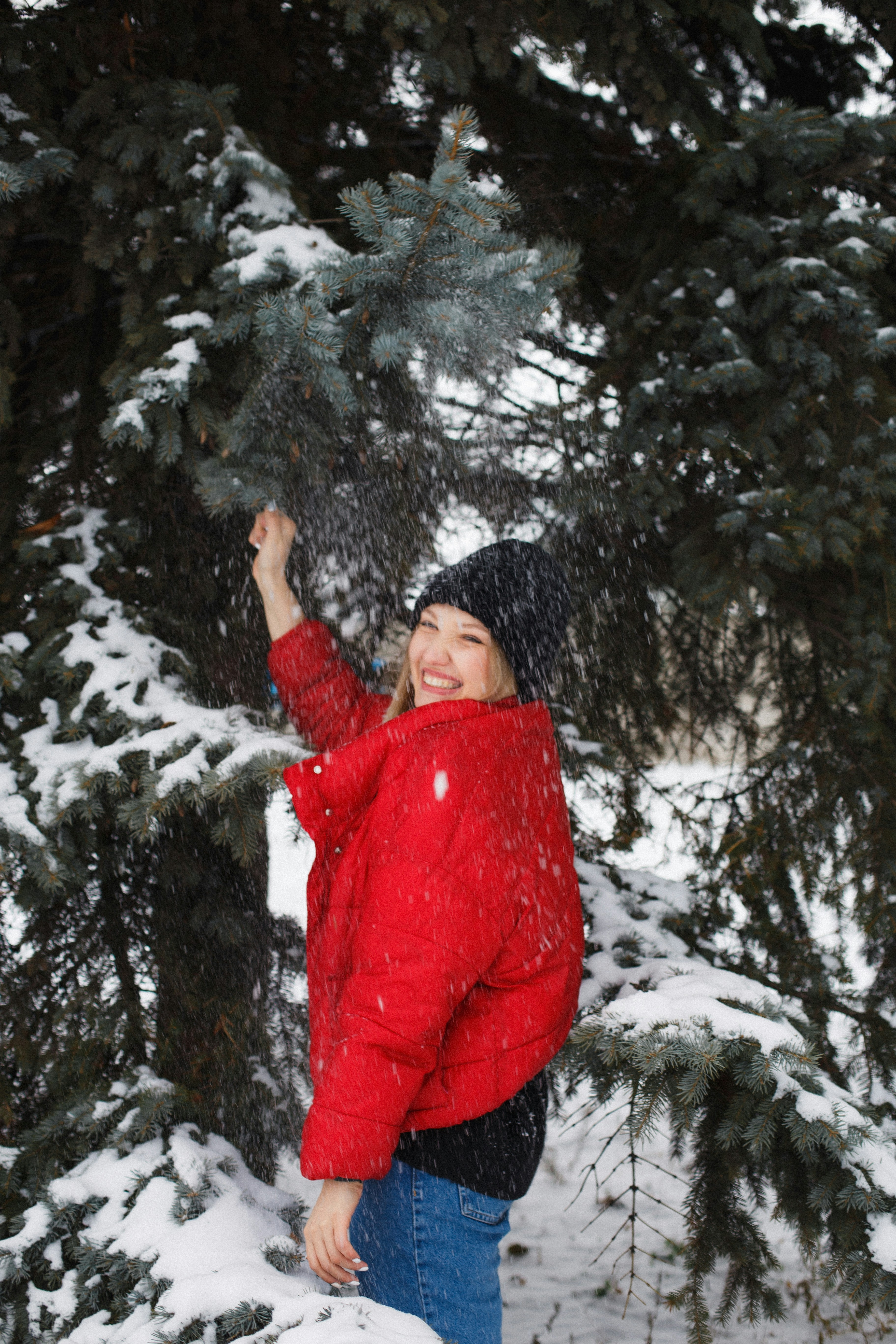 woman in red jacket standing near trees covered with snow