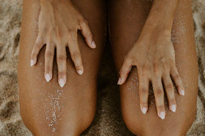 Close-up of intertwined hands resting on soft sand, bathed in warm afternoon sun.
