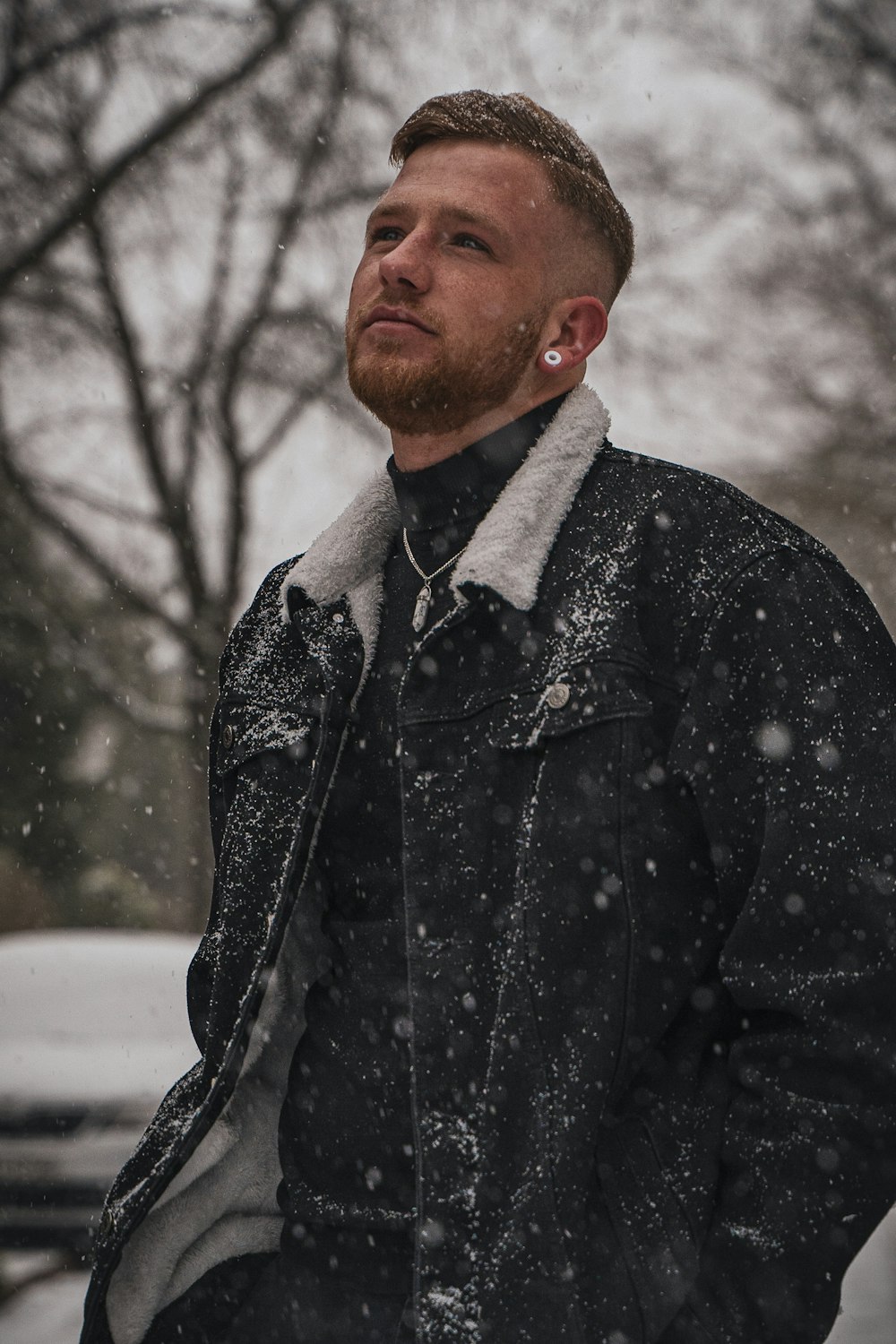 homem em jaqueta de botão preto e cinza em pé no chão coberto de neve durante o dia