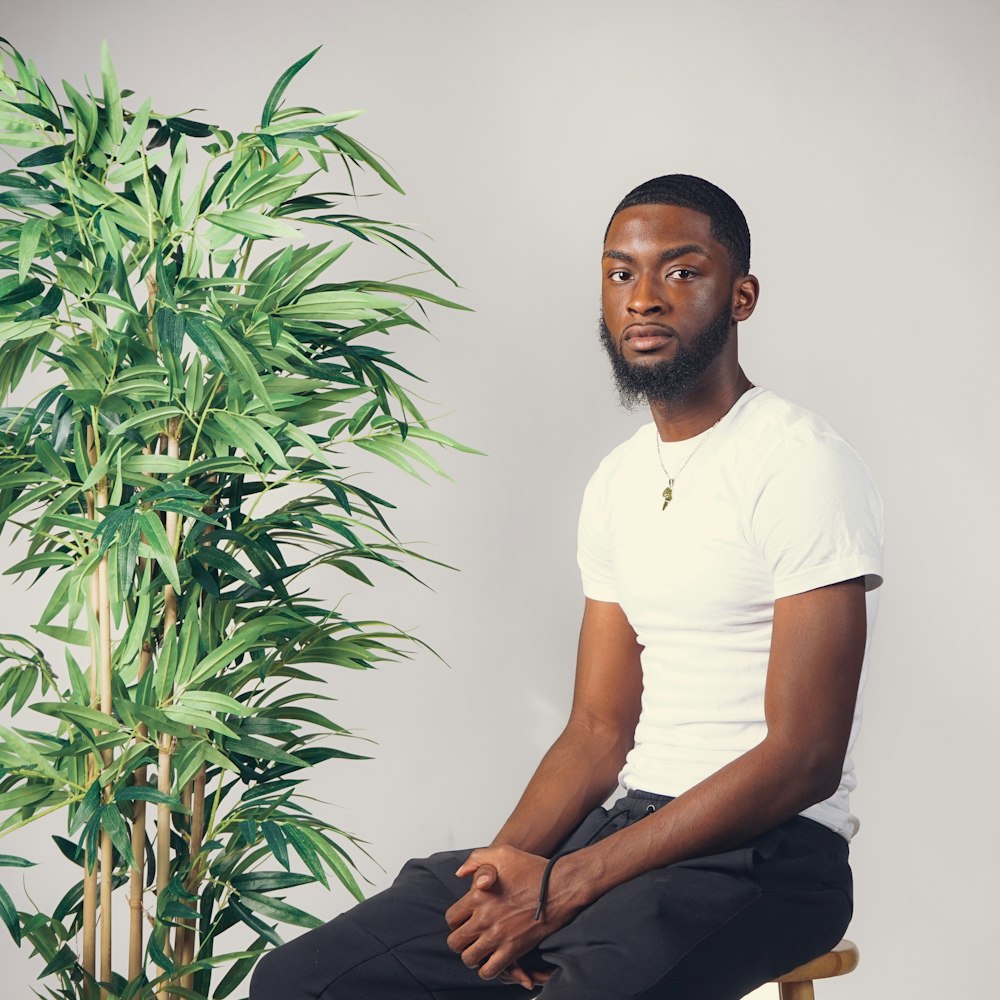 man in white crew neck t-shirt and black pants sitting on white wall