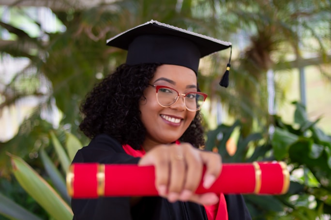 Graduate woman in cap and glasses holding a red diploma, illustrating academic accomplishment