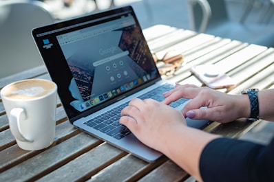 person using macbook pro on brown wooden table