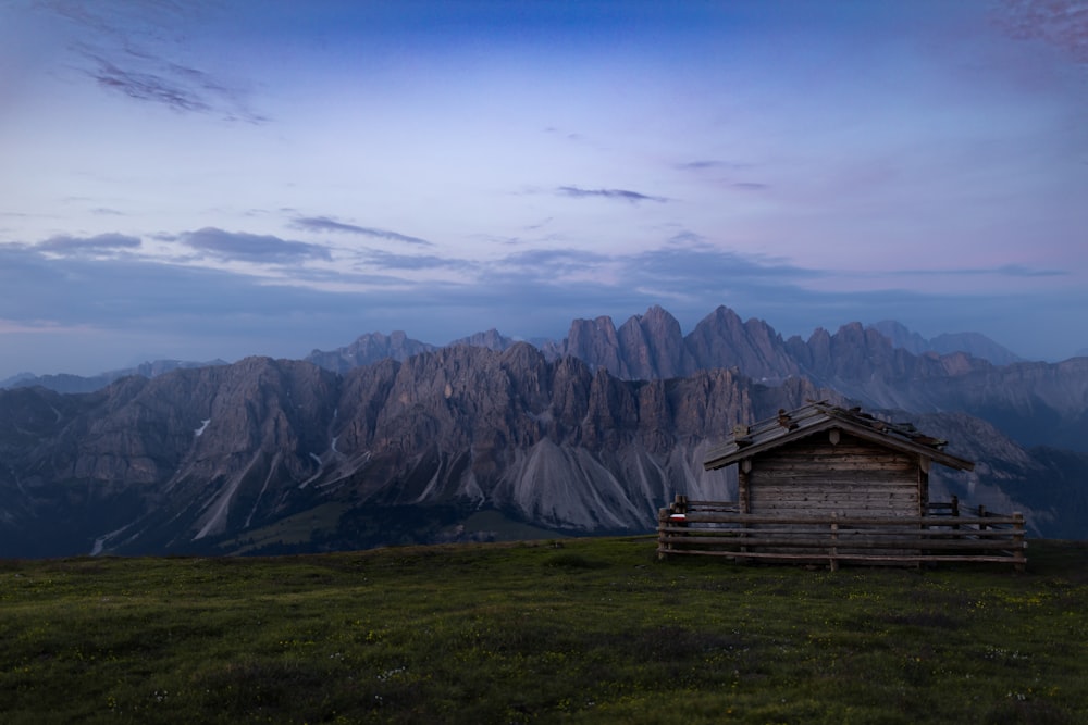 brown wooden house on green grass field near mountains under blue sky during daytime