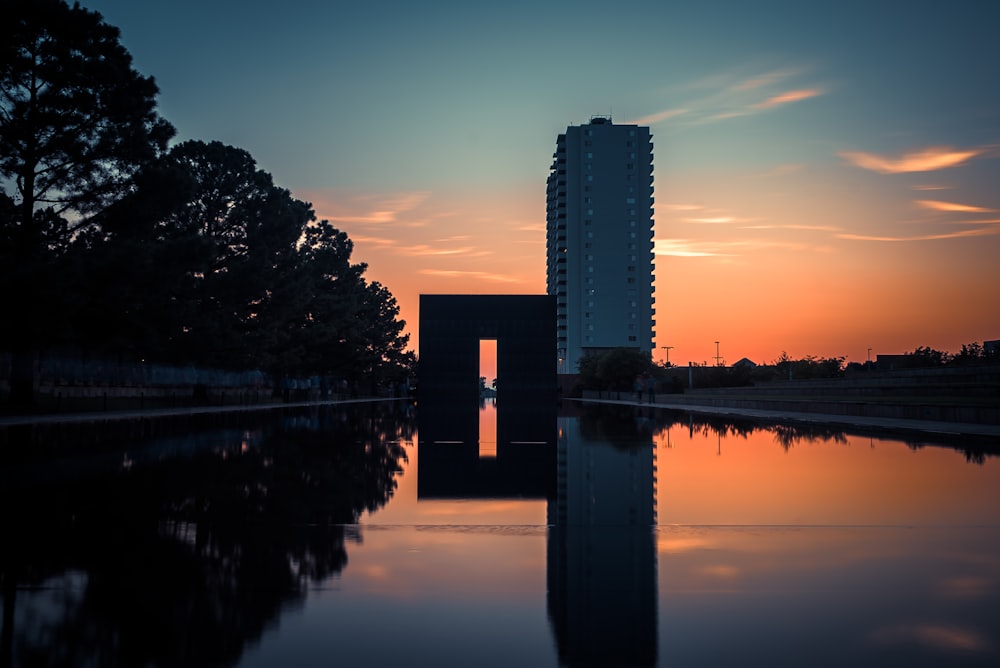Specchio d'acqua vicino agli alberi e al grattacielo durante il tramonto